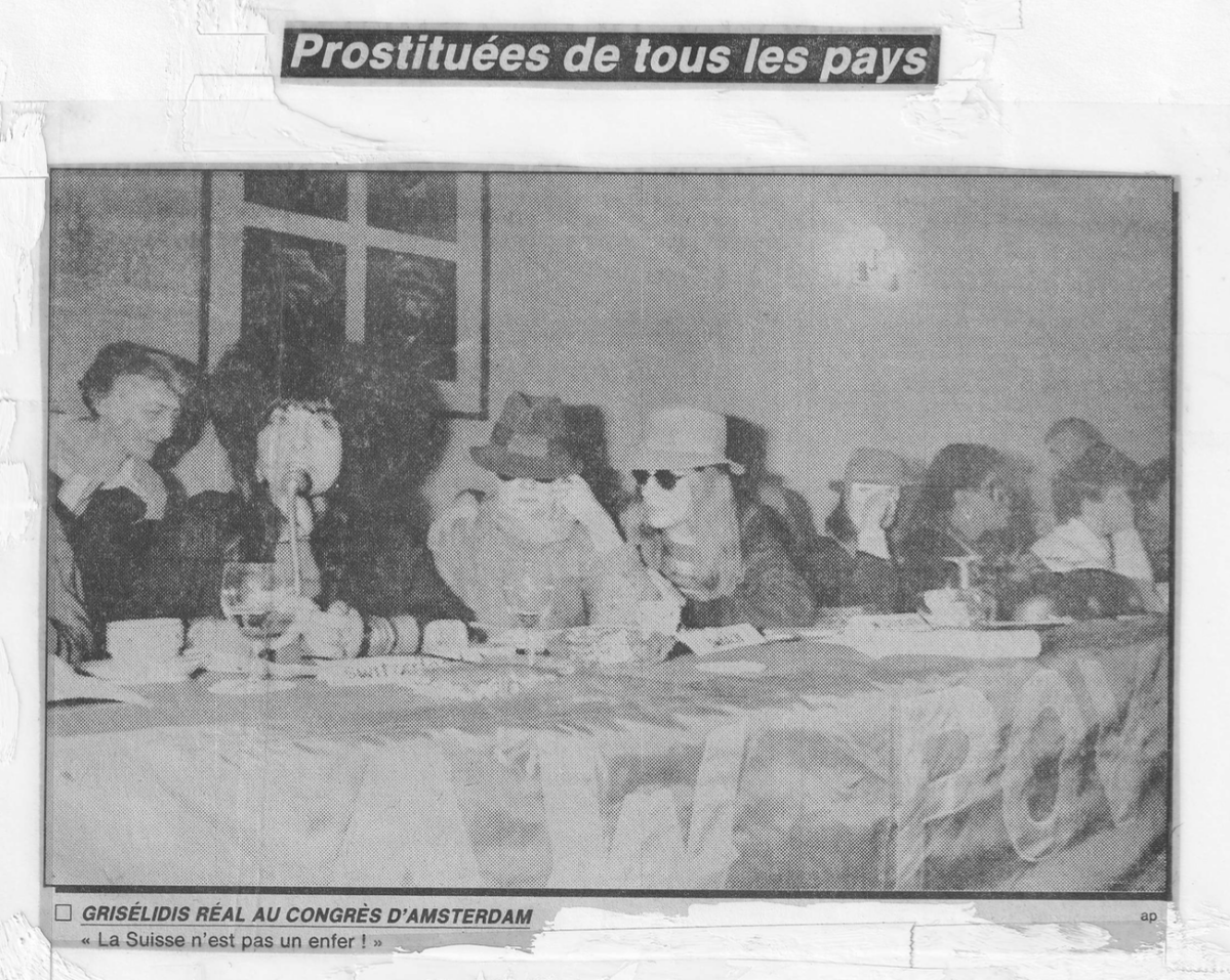 Schriftzug "Prostituées de tous les pays" mit Foto von Personen an einem Tisch.